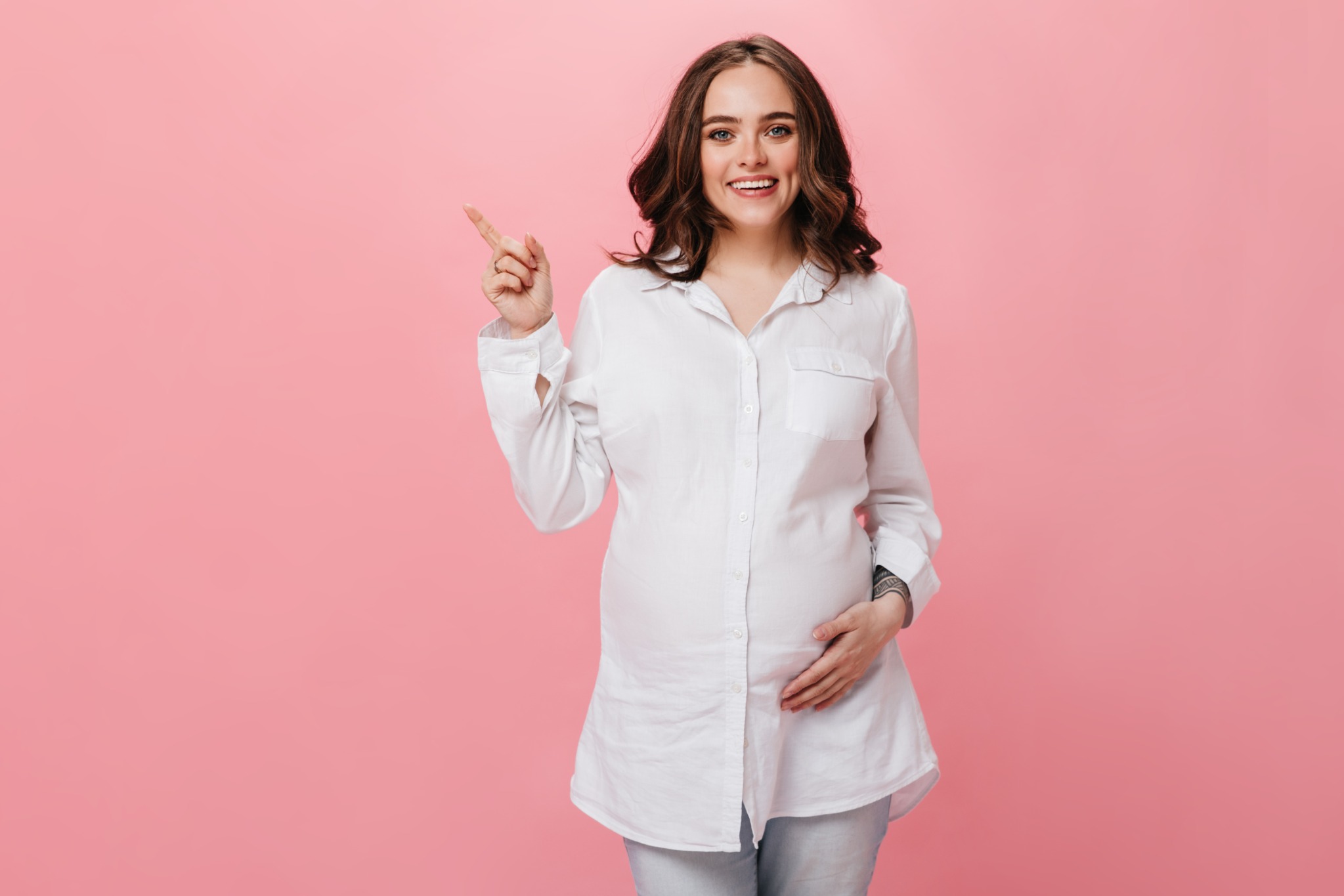 Gestante sorrindo e apontando sobre fundo rosa